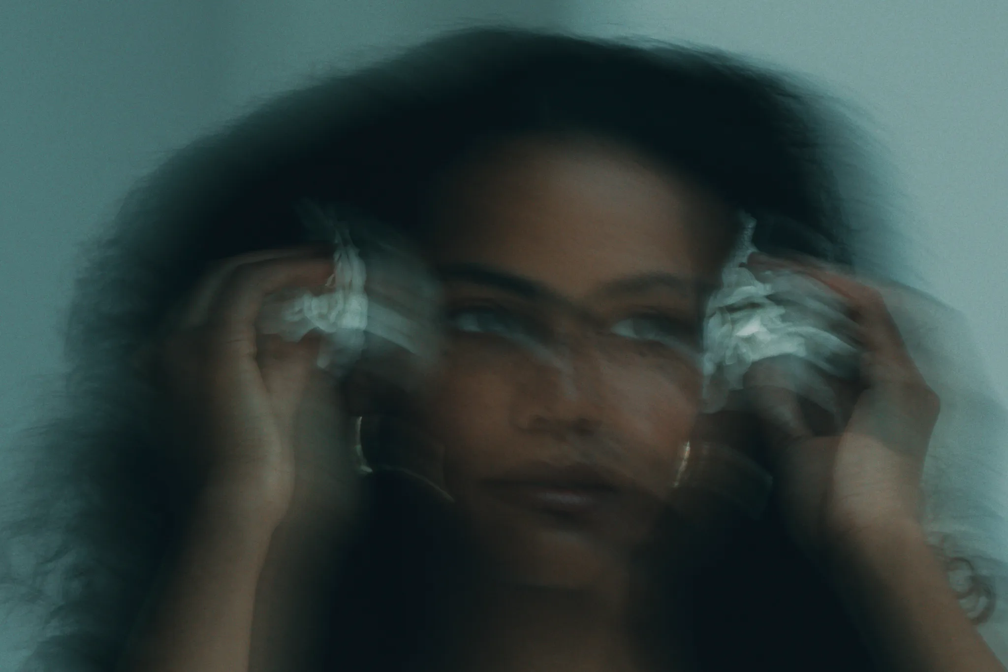 Blurred image of a person with hands near their face, creating a double-exposure effect.