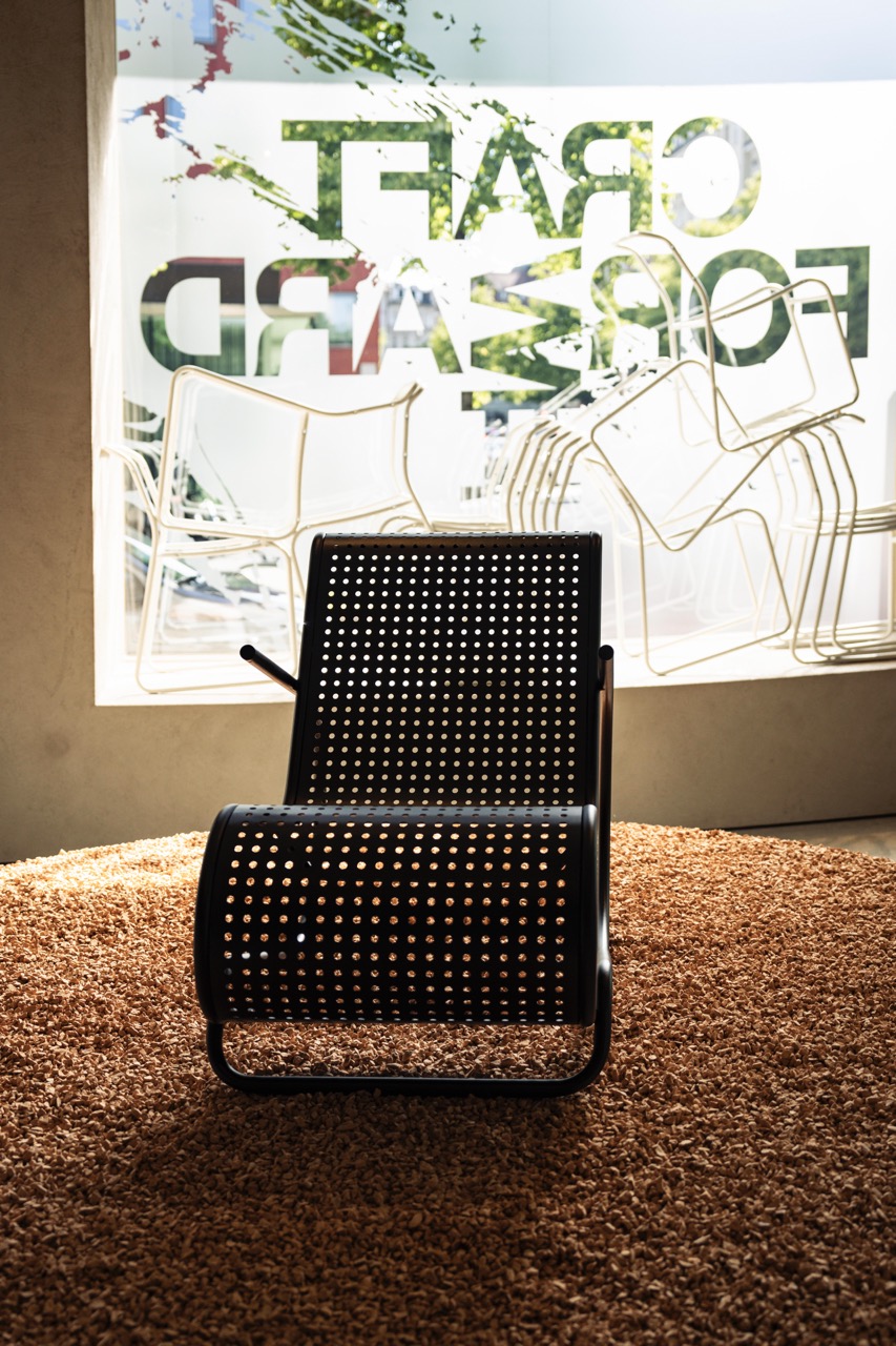 Showroom with a black mesh chair on a round wood-chip platform and Craft Forward window lettering. Event photography by FADETOBLACK