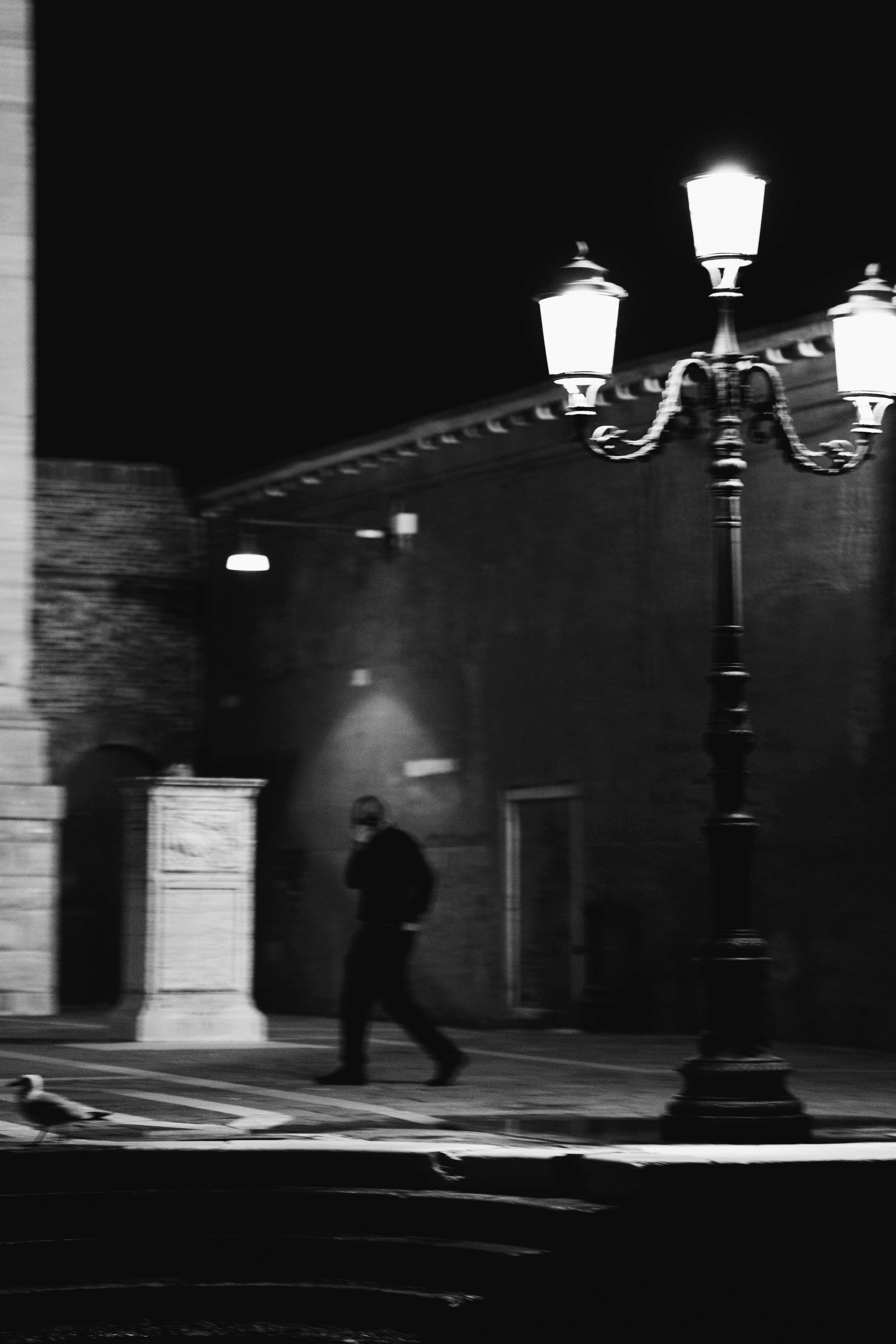 Venice in the Shadows by FADETOBLACK, fine art street photography, image 7: High-contrast black and white night scenes in Venice: a lone man walking across a dark square past an ornate