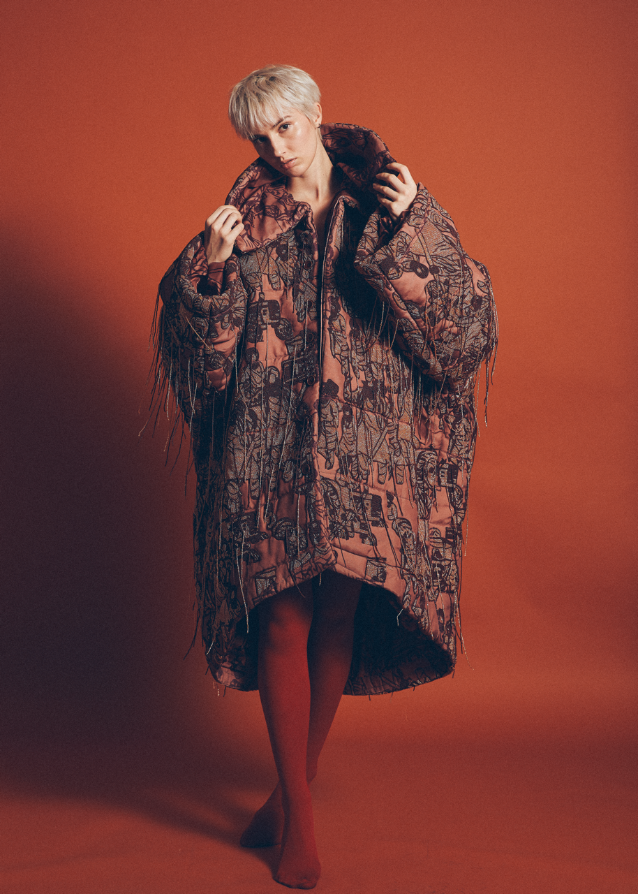 Jaang by FADETOBLACK, editorial fashion photography, image 15: Studio fashion editorial of a model with short platinum hair wearing avant-garde statement pieces, including