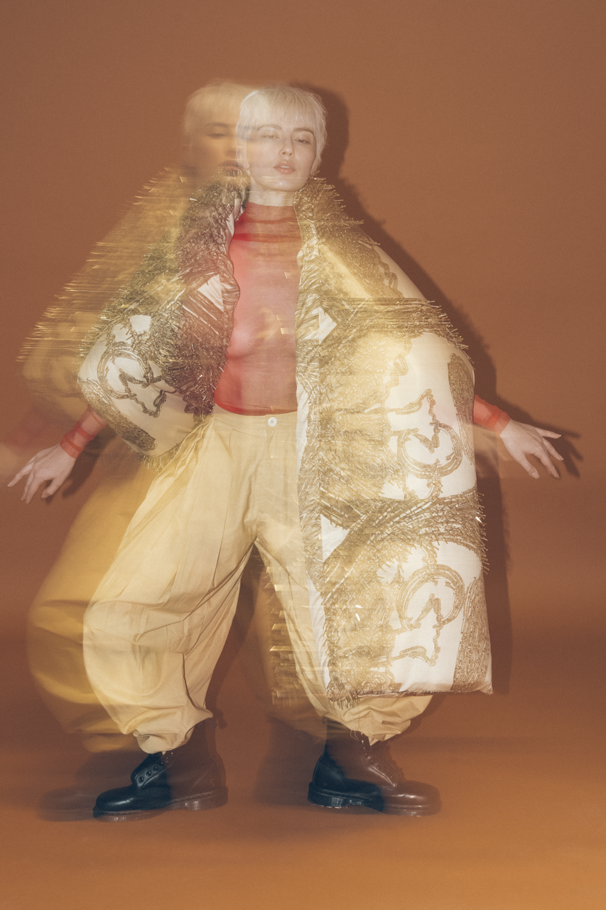 Jaang by FADETOBLACK, editorial fashion photography, image 20: Studio fashion editorial of a model with short platinum hair wearing avant-garde statement pieces, including