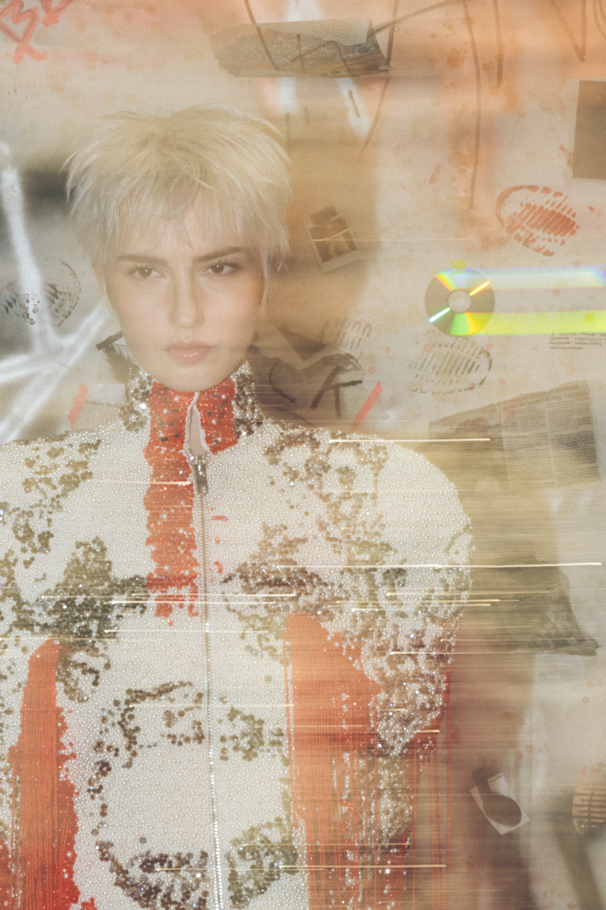 Jaang by FADETOBLACK, editorial fashion photography, image 24: Studio fashion editorial of a model with short platinum hair wearing avant-garde statement pieces, including