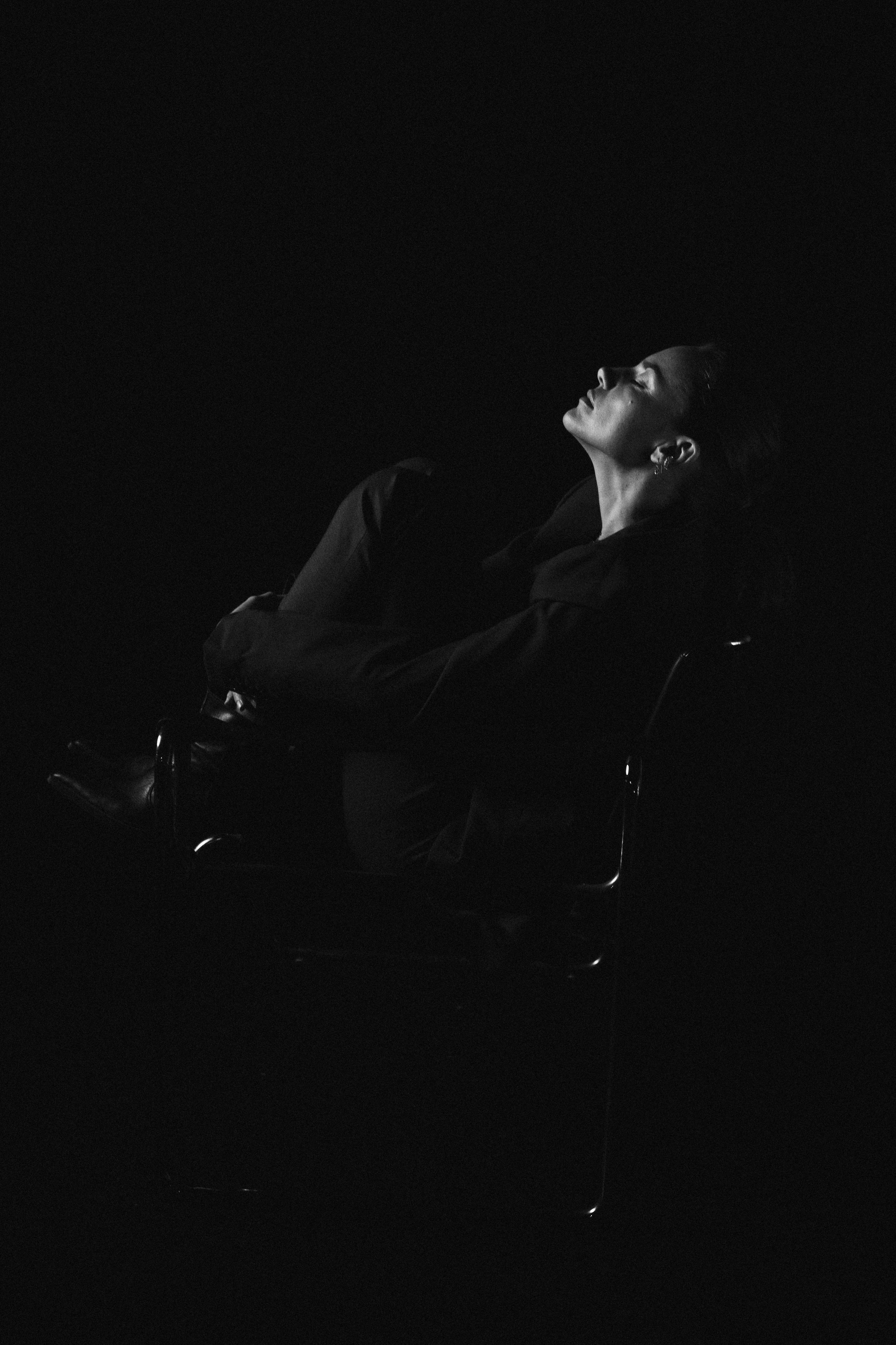 Hanna: The Transformation by FADETOBLACK, fine art portrait photography, image 8: Low-key black and white studio portrait series of a woman in a dark suit posing on and around a chrome-framed