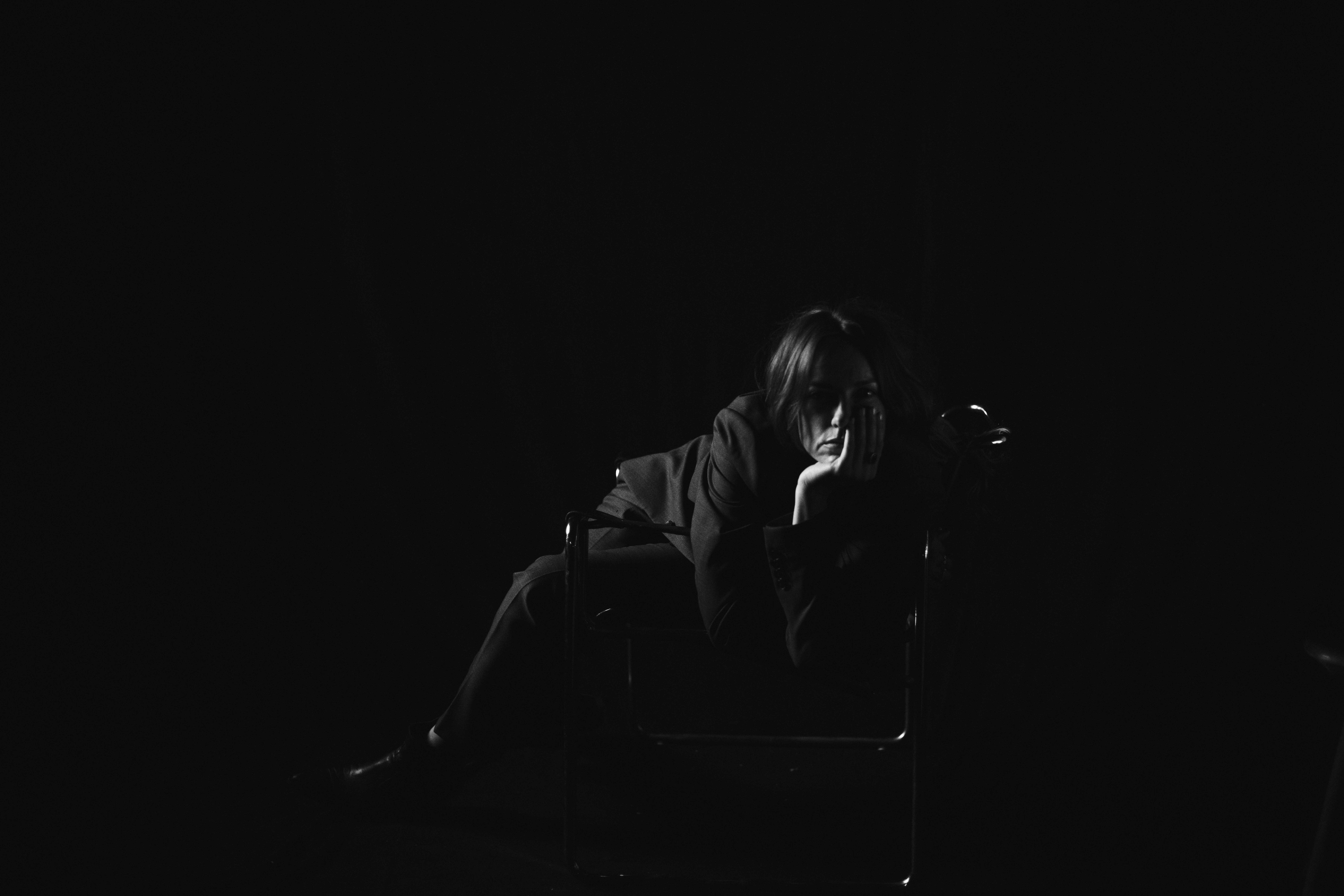 Hanna: The Transformation by FADETOBLACK, fine art portrait photography, image 19: Low-key black and white studio portrait series of a woman in a dark suit posing on and around a chrome-framed