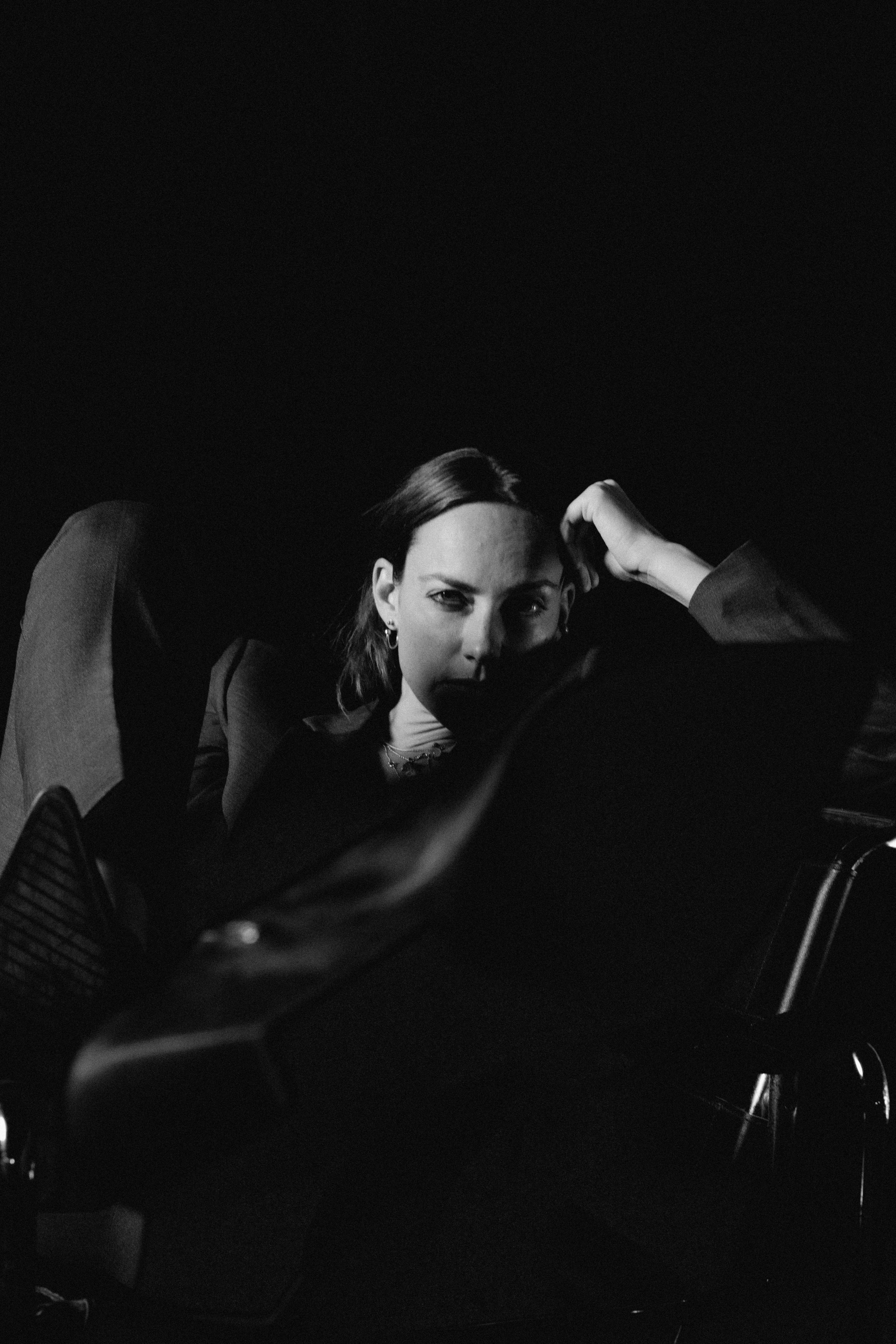 Hanna: The Transformation by FADETOBLACK, fine art portrait photography, image 13: Low-key black and white studio portrait series of a woman in a dark suit posing on and around a chrome-framed