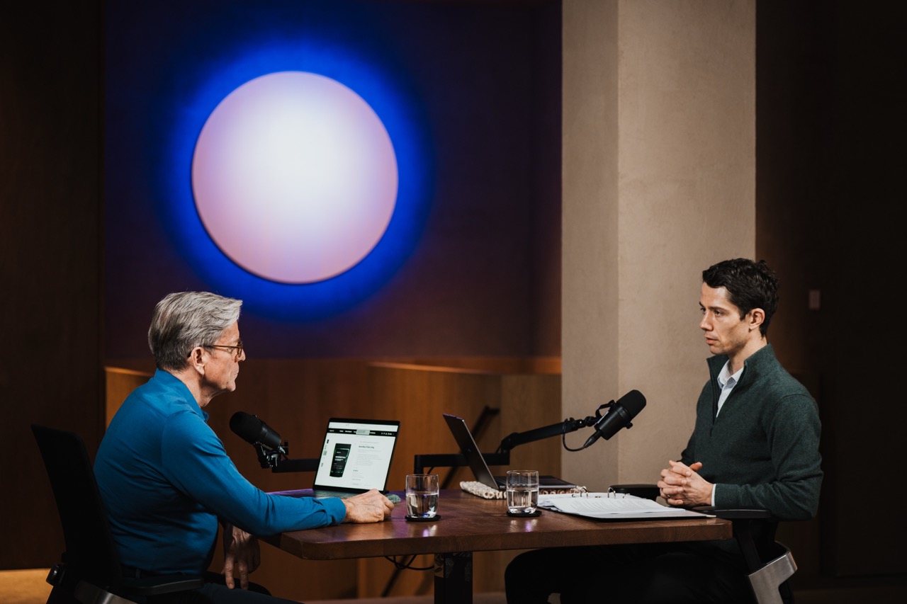 Two men recording a podcast episode in a studio with a blue backdrop, symbolic image for podcast production costs, FADETOBLACK Munich