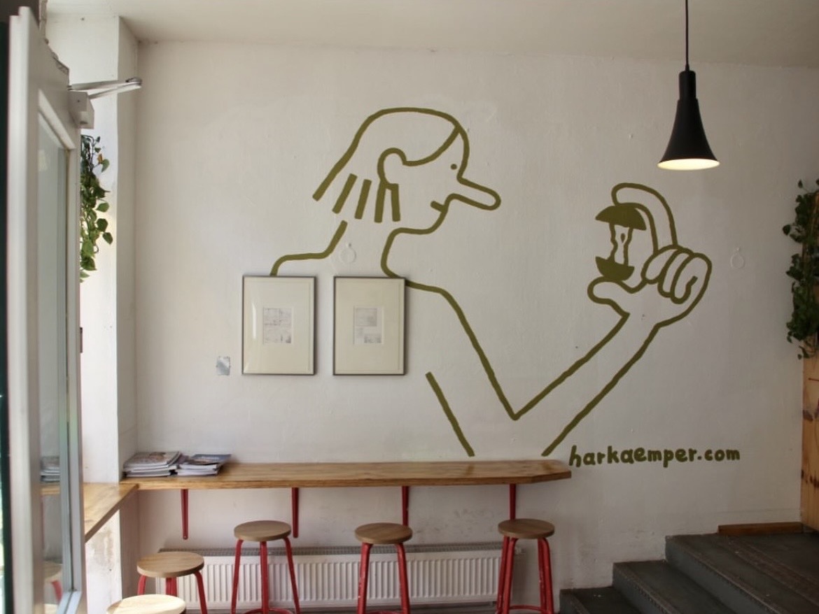 Interior of a cafe with a wooden counter and red stools under a wall mural of a person holding an apple.