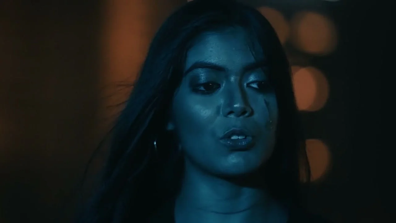 Disha Bhattacharjee as Deepa in Kali, her face lit in deep blue against warm lights.