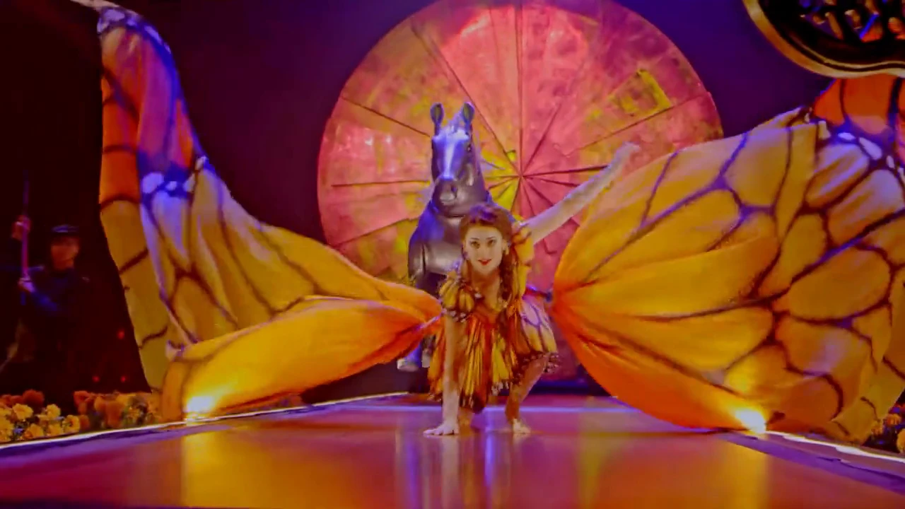 A performer spreads butterfly wings across the vividly lit Luzia stage.
