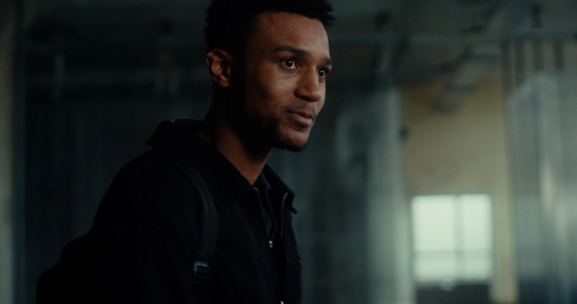 Nathan looks across the workshop in Indispensable, his face lit by a cool window