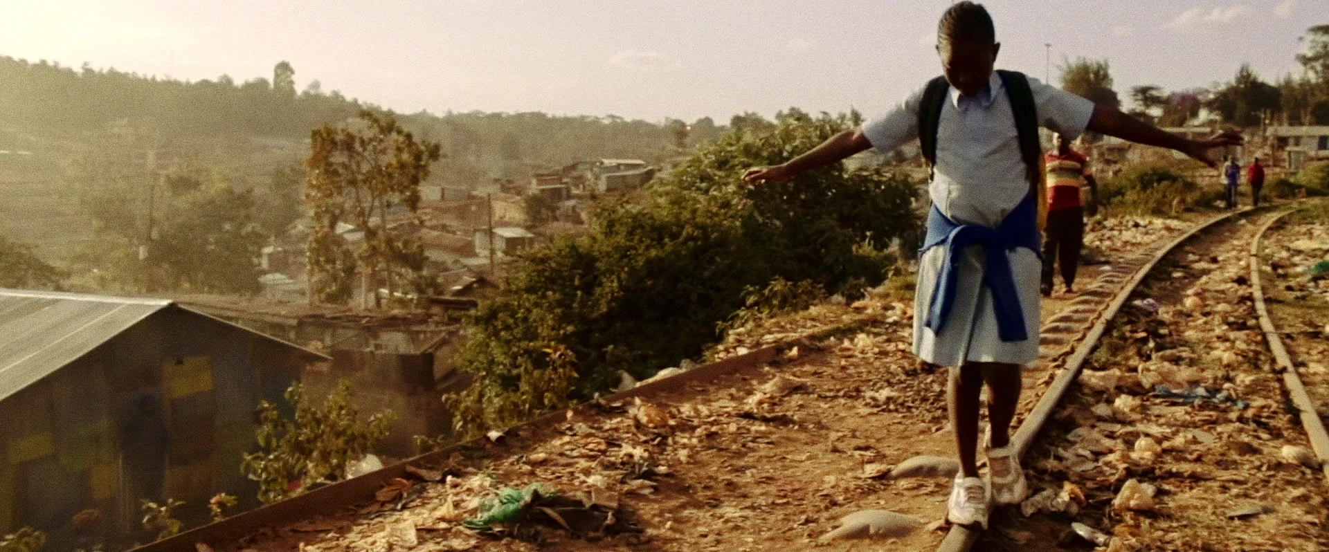 A schoolgirl balances along railway tracks above Nairobi in warm afternoon light