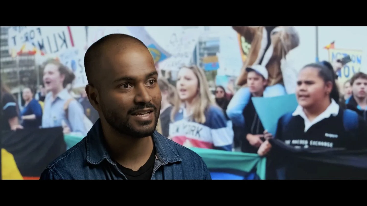 Soumik Datta speaks in the Silent Spaces documentary, with an image of a climate march behind him