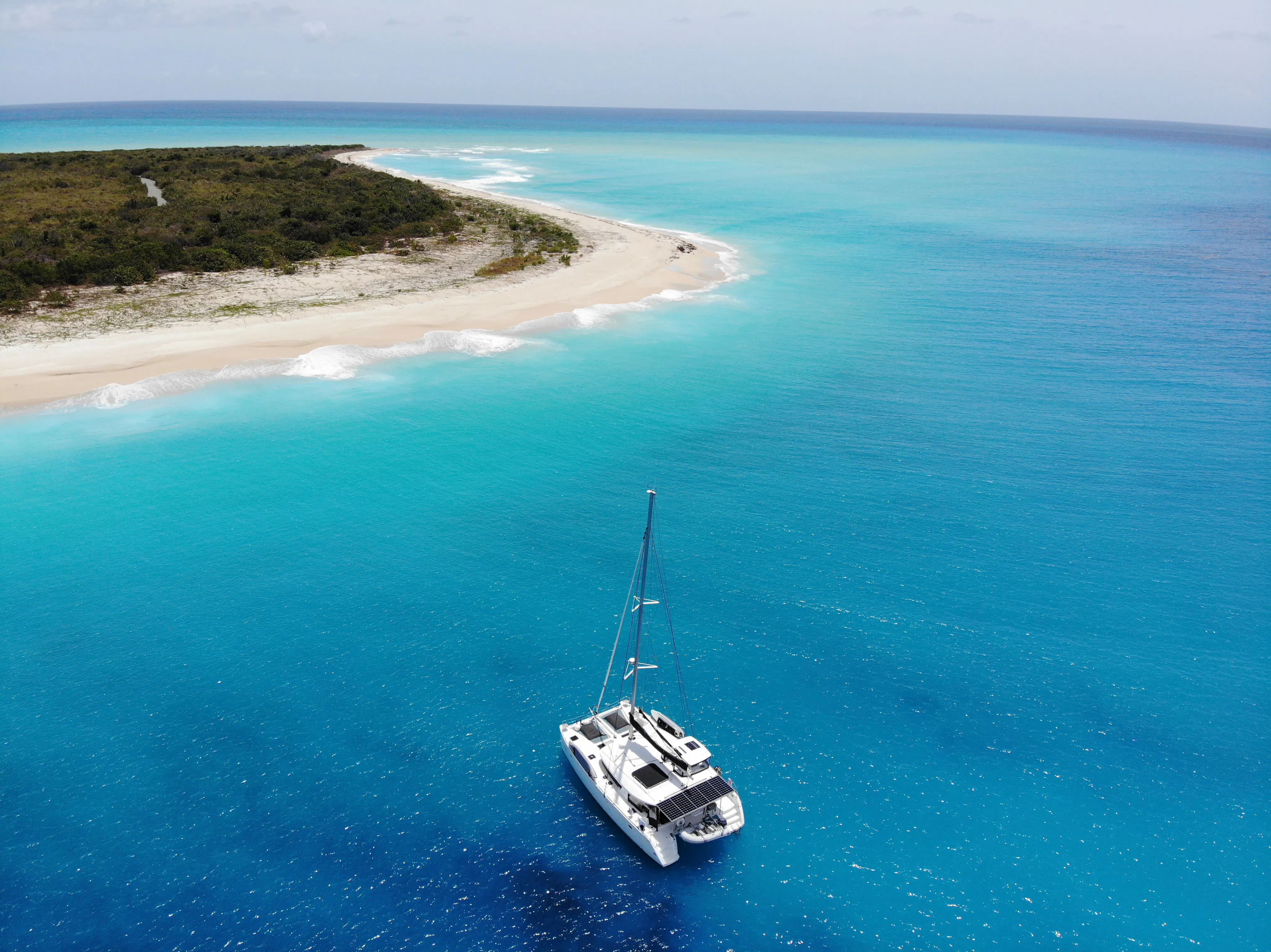 Aerial view of a crewed yacht anchored in clear blue water beside a Caribbean island
