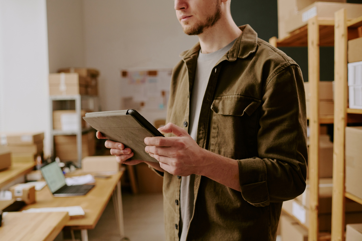 A man in a warehouse holds an ipad checking on statistics and KPIs