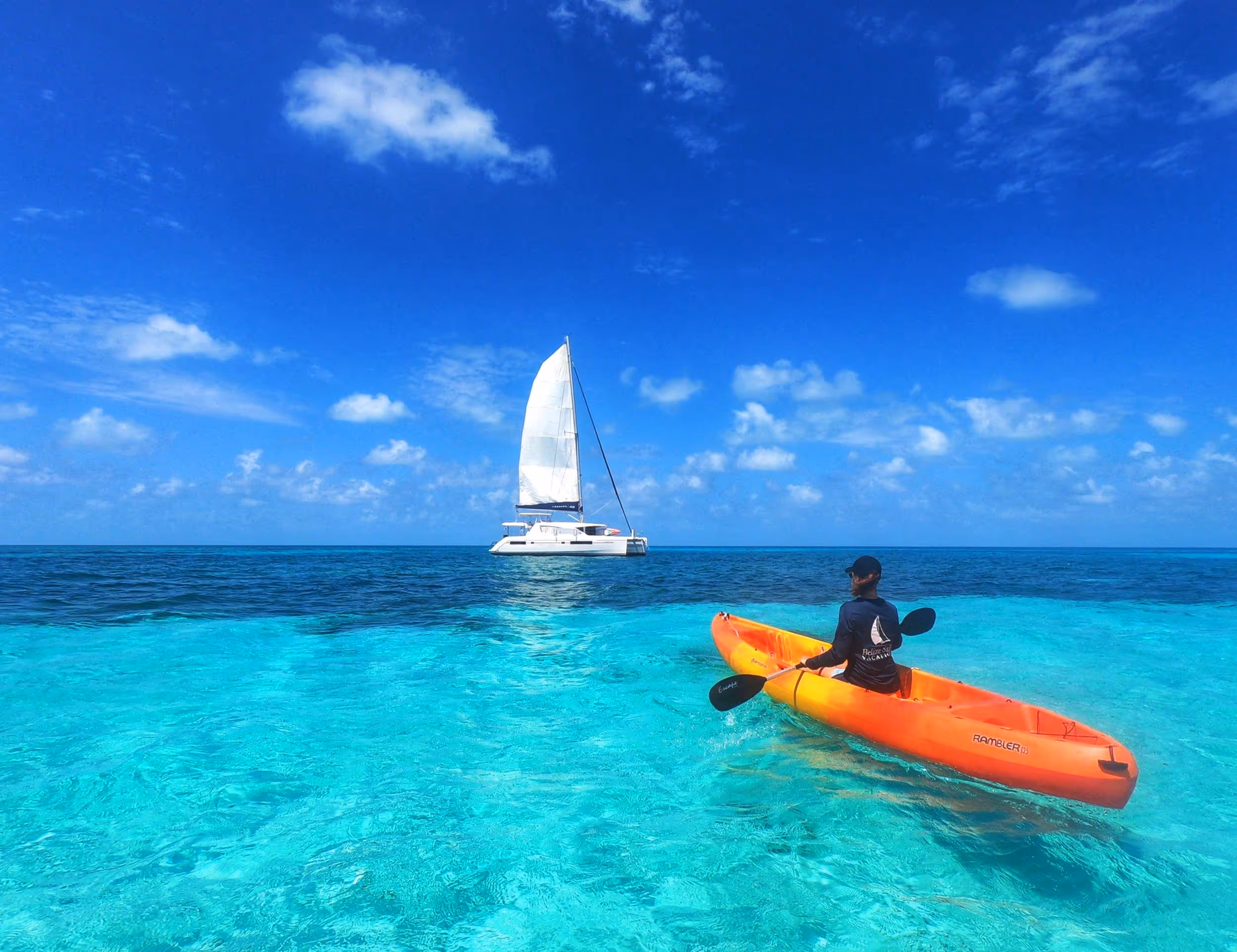 Guest kayaking in turquoise water with the catamaran at anchor