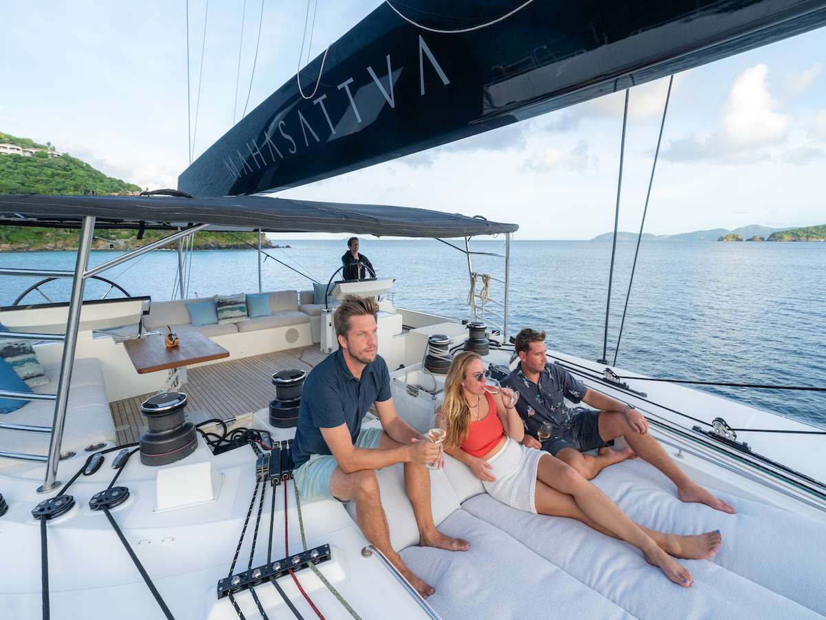 Three guests relaxing on the bow of a sailing catamaran