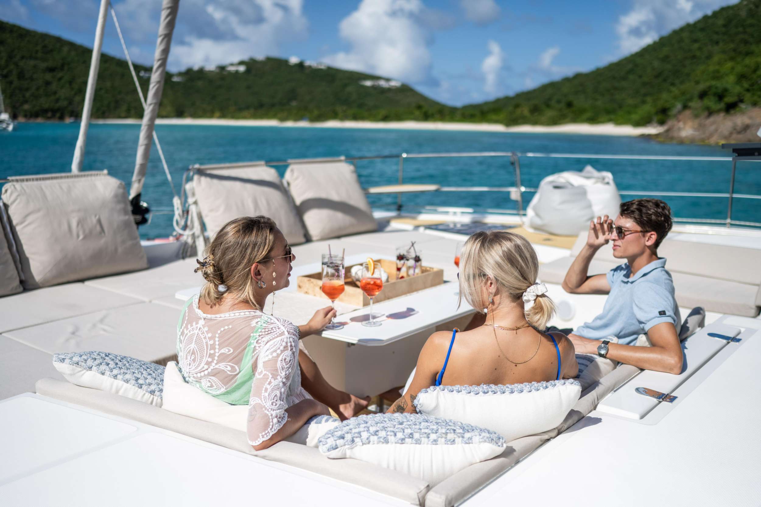 Three friends sharing drinks at the foredeck table of a crewed catamaran