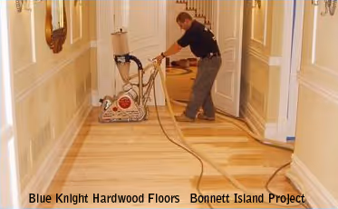 Worker refinishing hardwood floor in a hallway using sanding equipment.