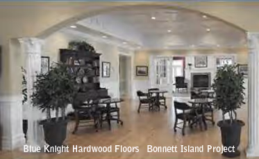 Spacious room with light hardwood floors, black wooden tables and chairs, potted plants, and an archway with white columns.