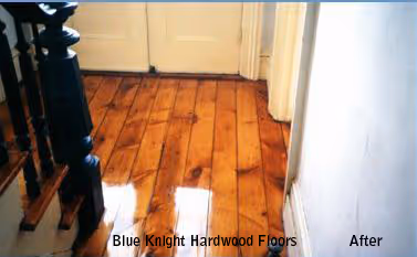Shiny, polished hardwood floor in a hallway with a staircase on the left and closed double doors ahead.