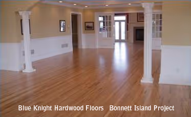 Spacious empty room with polished hardwood floors, white pillars, and beige walls.