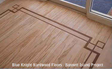 Close-up of hardwood floor with decorative inlaid wood border near a glass door.