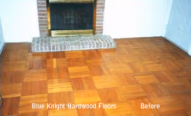 Wooden parquet floor with worn areas in front of a brick fireplace.
