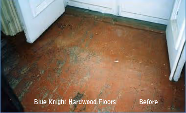 Worn and scratched hardwood floor in a corner room before refinishing.