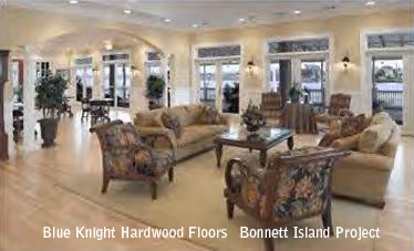 Spacious living room with hardwood floors, floral upholstered chairs, beige sofas, and large windows with outdoor views.