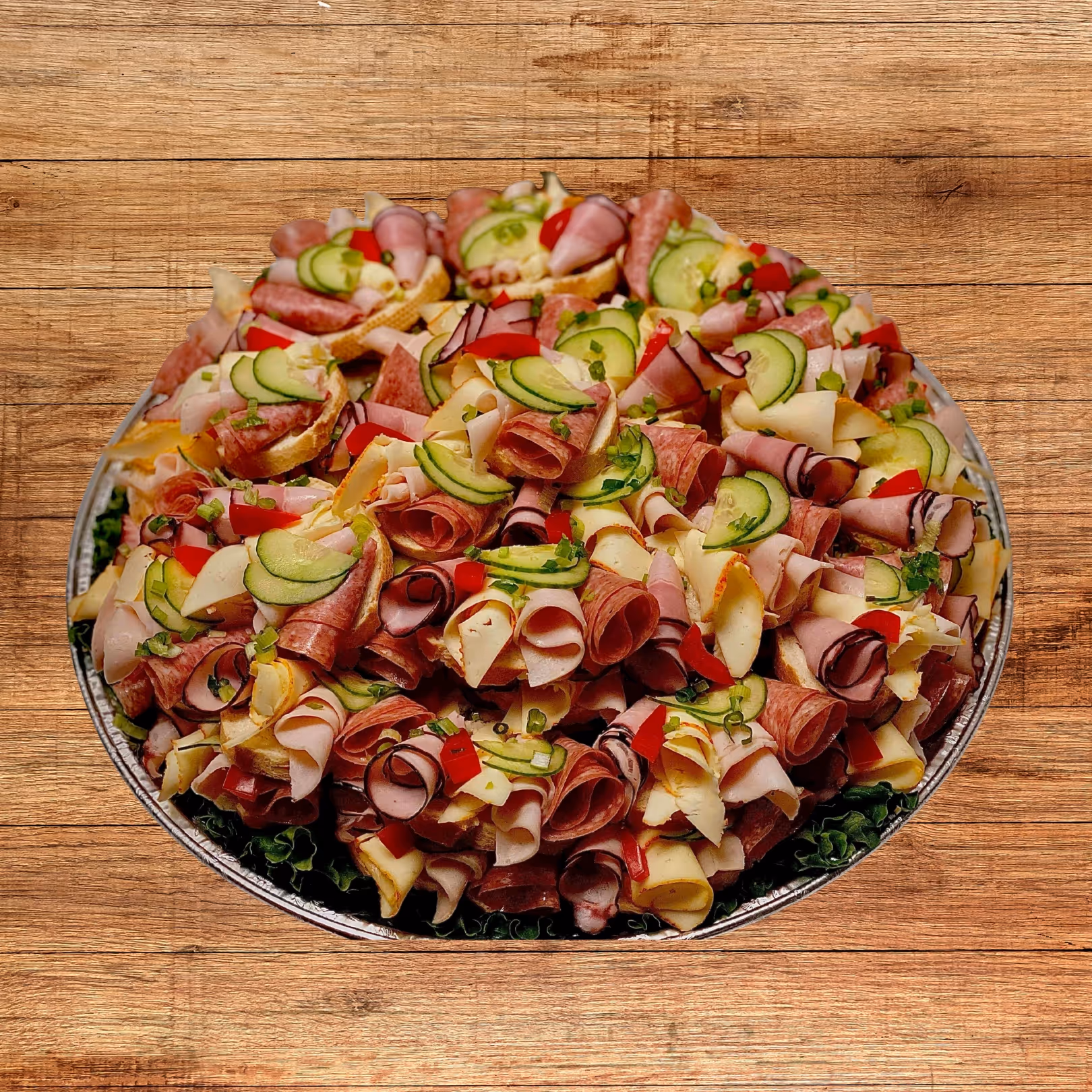 Large platter of assorted deli meats and cheeses garnished with cucumber slices, red bell peppers, and green onions on a bed of lettuce.