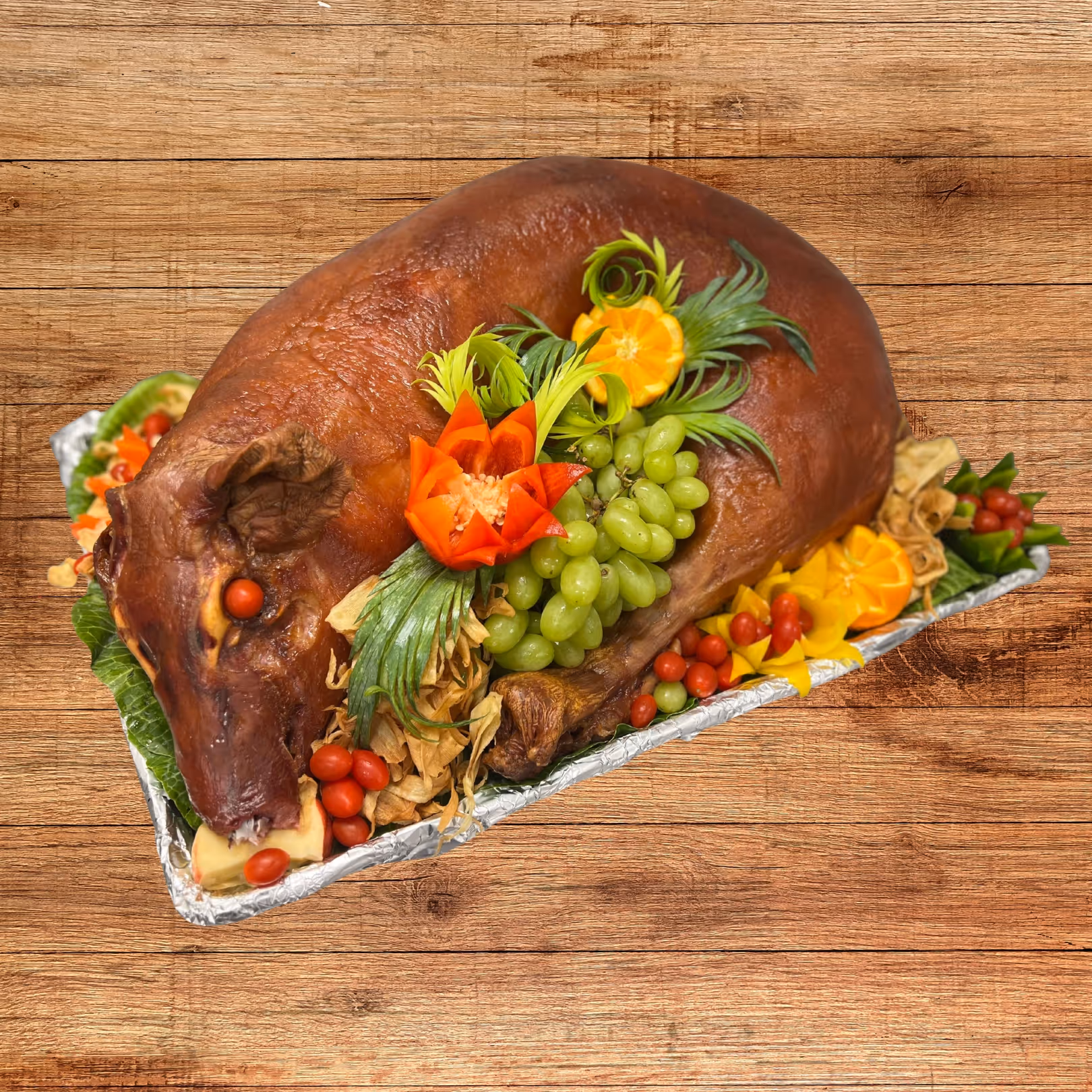 Whole roasted pig garnished with green grapes, cherry tomatoes, orange slices, and leafy greens on a serving tray.