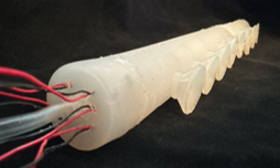 Close-up of a translucent silicone tube with multiple red and black wires emerging from one end, lying on a dark surface.