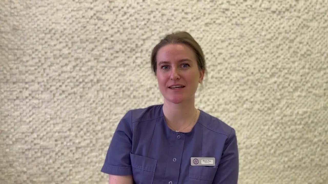 A woman in scrubs sitting in front of a wall.