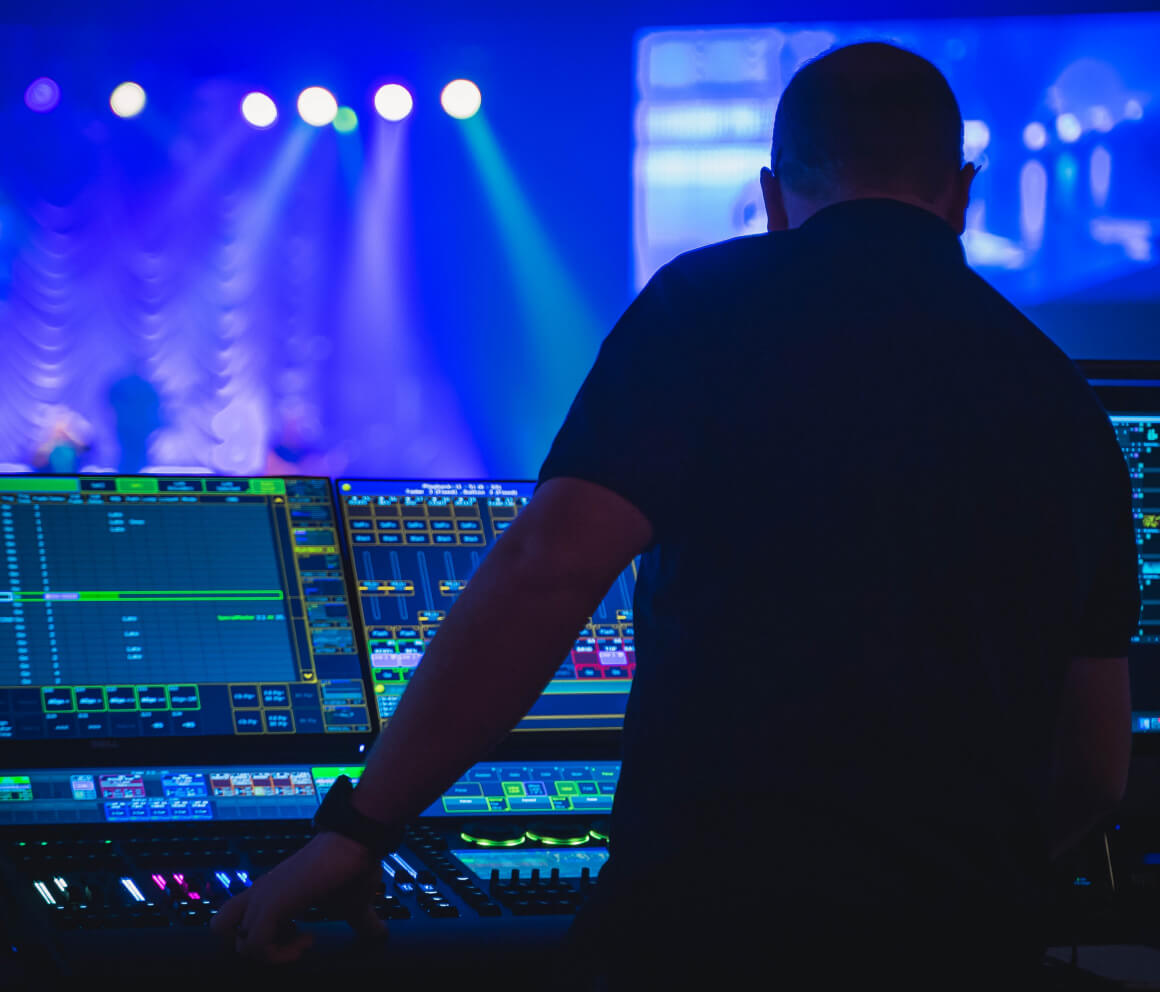 A live sound engineer working while music artists perform in the background