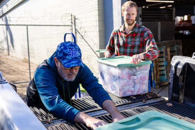 Two gentleman loading backpacks for children into a truck.