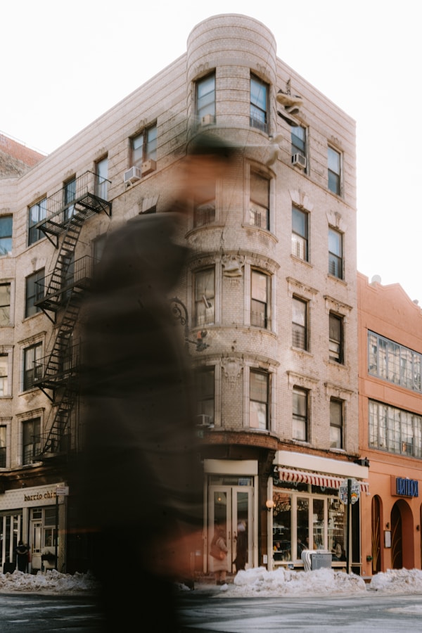 Blurry figure walks past a building with fire escape.