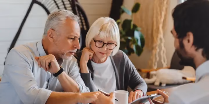 An elderly couple reviewing documents with a financial advisor at a table.