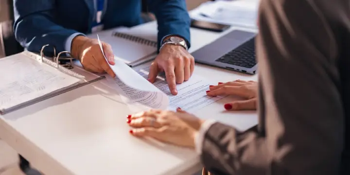 A lawyer meeting with a client to discuss a will dispute, holding notes and a pen during the consultation.