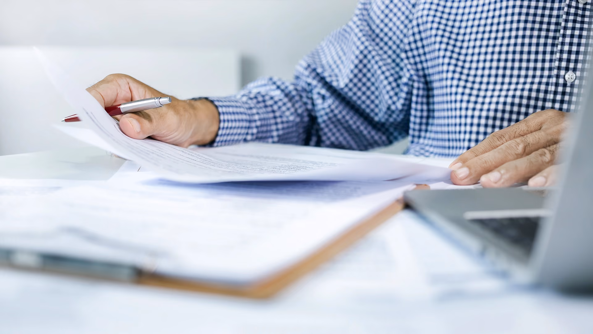 Person reviewing divorce application papers at home while holding a pen beside a laptop and paperwork on a desk.