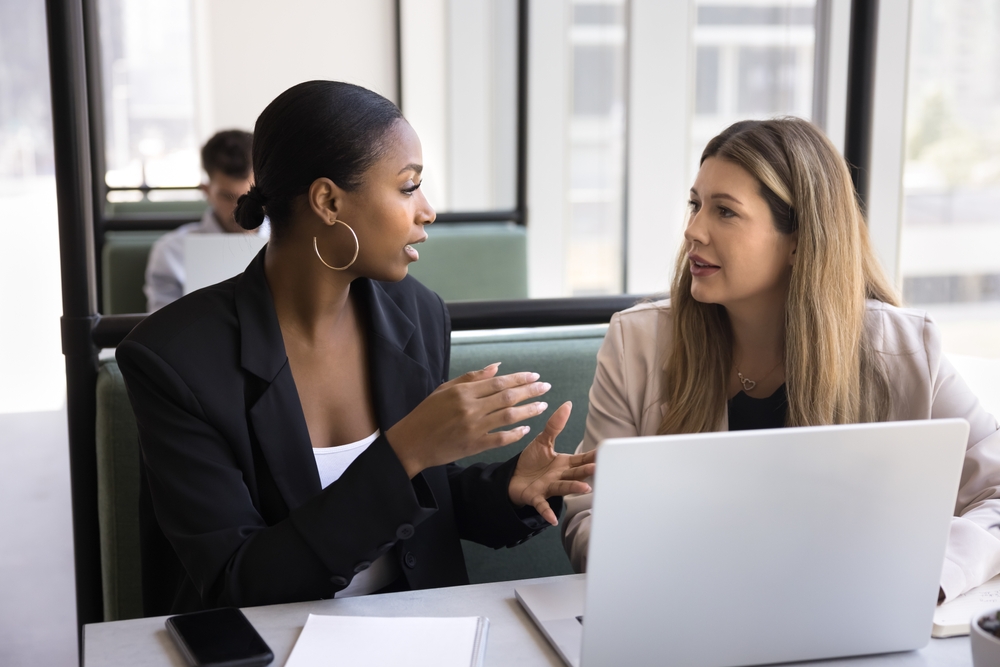 Two women sitting at a desk with legal documents, discussing and signing paperwork related to a will dispute.