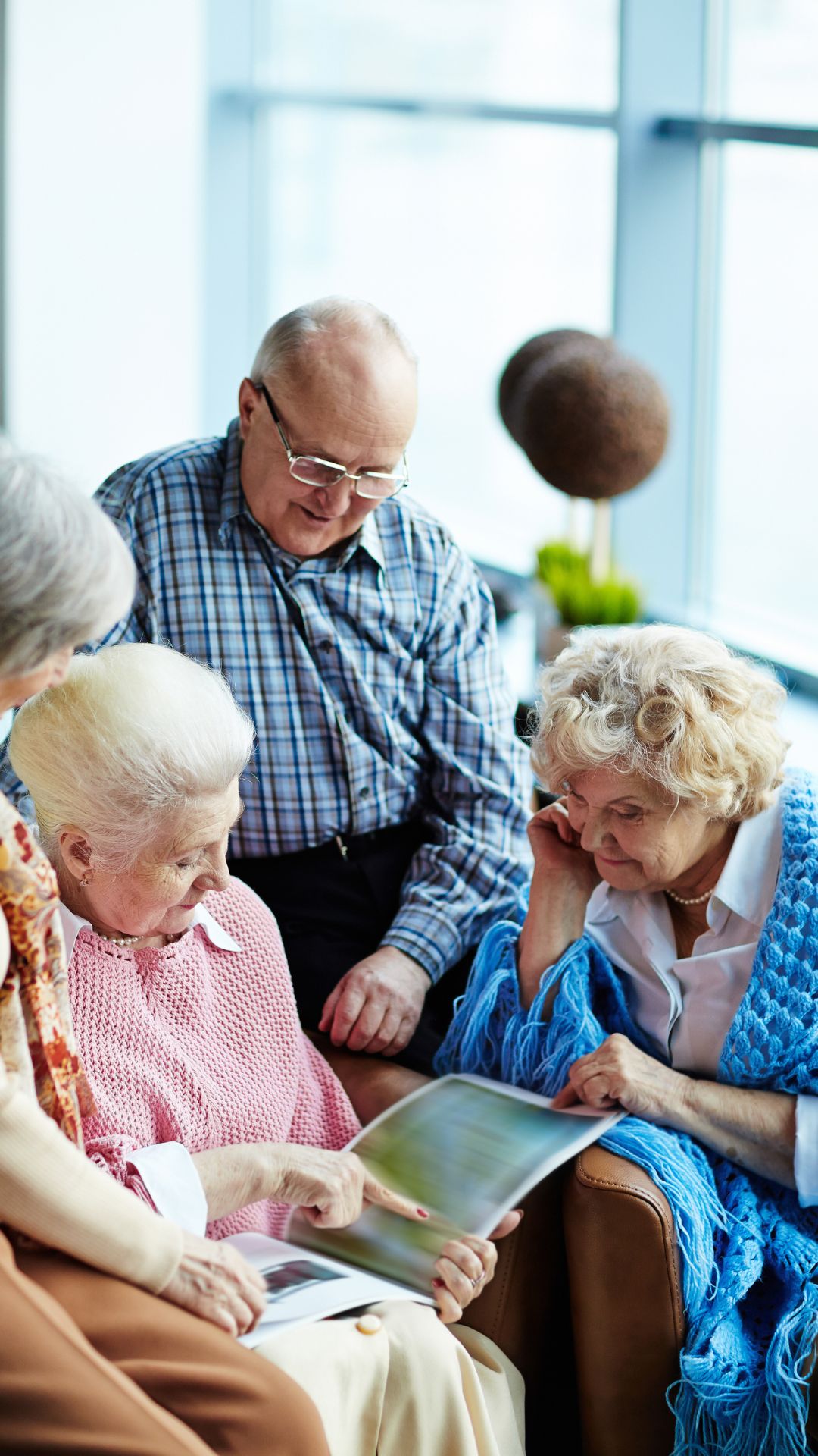 Group of elderly people sitting together and looking at a photo album indoors.