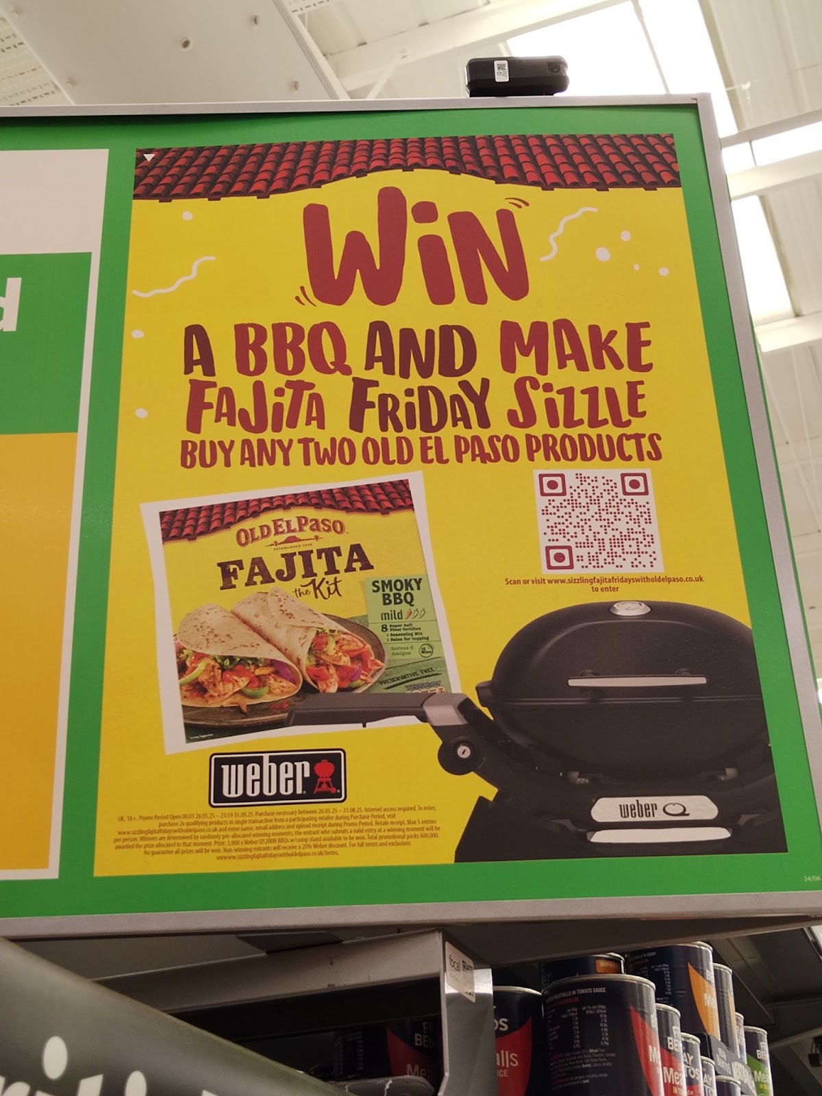 Overhead sign for Old El Paso. Text reads: "Win // A BBQ AND MAKE // Fajita Friday Sizzle // BUY ANY TWO OLD EL PASO PRODUCTS". Sign features a QR code, an image of a Weber grill, and small text with promotional rules.