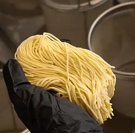Hand wearing a black glove holding a bundle of fresh yellow noodles.