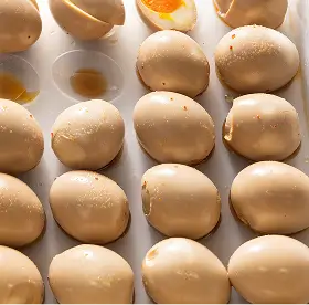 Rows of shiny caramel-coated round confections with a glossy finish, some with visible soft orange centers.