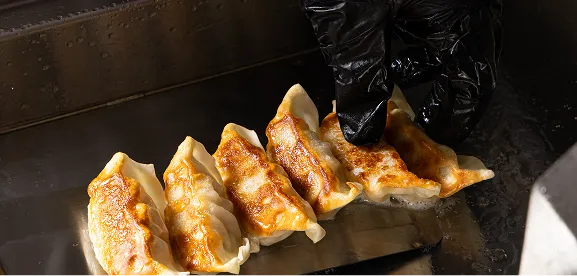 Gloved hand flipping golden-brown pan-fried dumplings on a hot griddle.