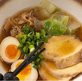 Bowl of ramen with sliced pork, soft-boiled eggs, green onions, mushrooms, and broth.