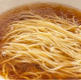 Close-up of noodles submerged in clear brown broth with visible oil droplets.