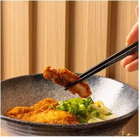 Hand holding chopsticks picking up a piece of fried chicken from a bowl with more fried chicken and chopped green onions.