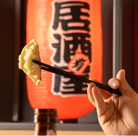 Hand holding chopsticks picking up a dumpling with a red Japanese lantern in the background.