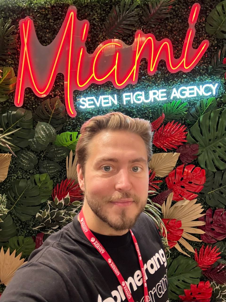 A Boomerang team member in front of a neon sign reading Miami over Seven Figure Agency